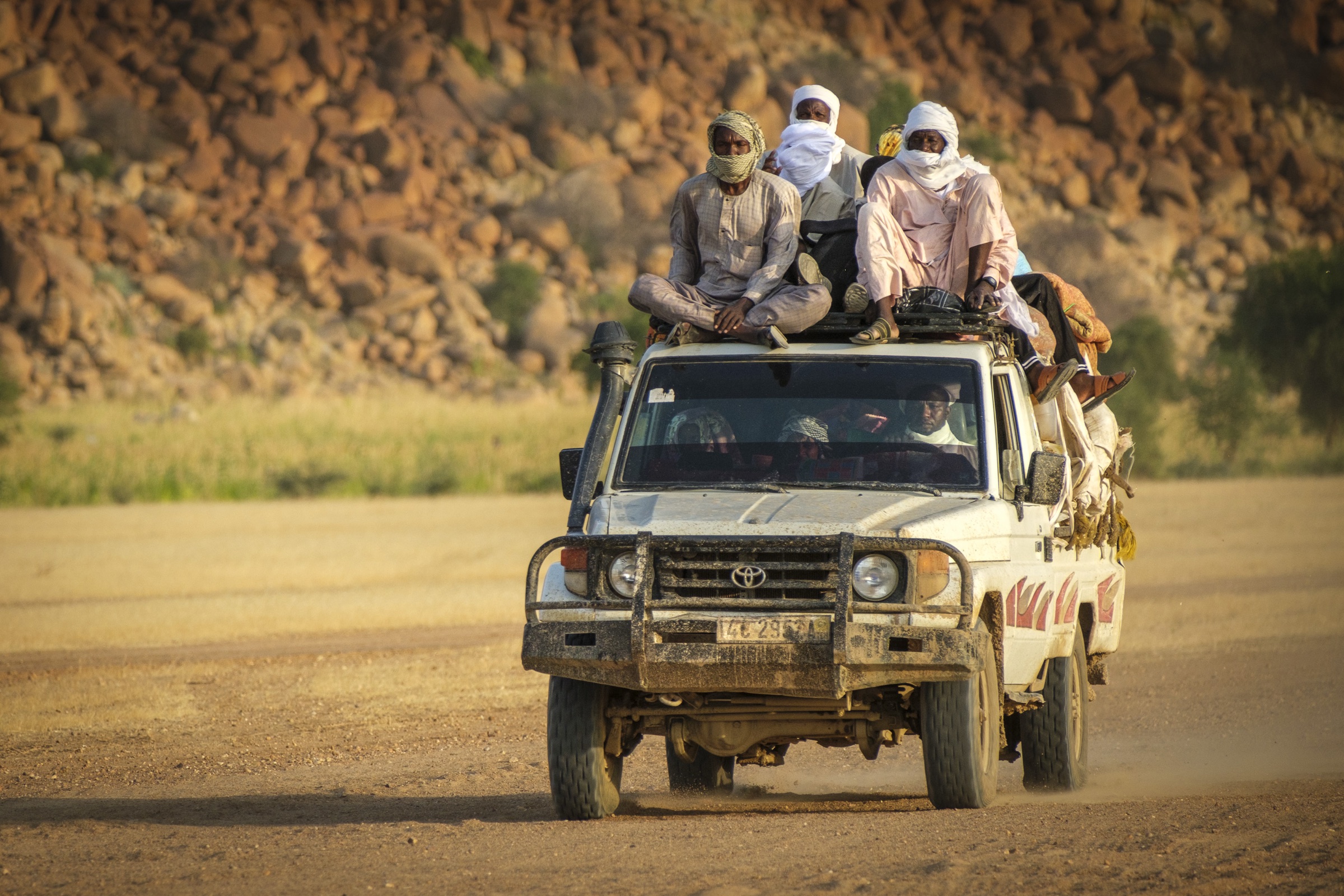 People riding on top of a loaded pickup truck on a dirt road in Chad.