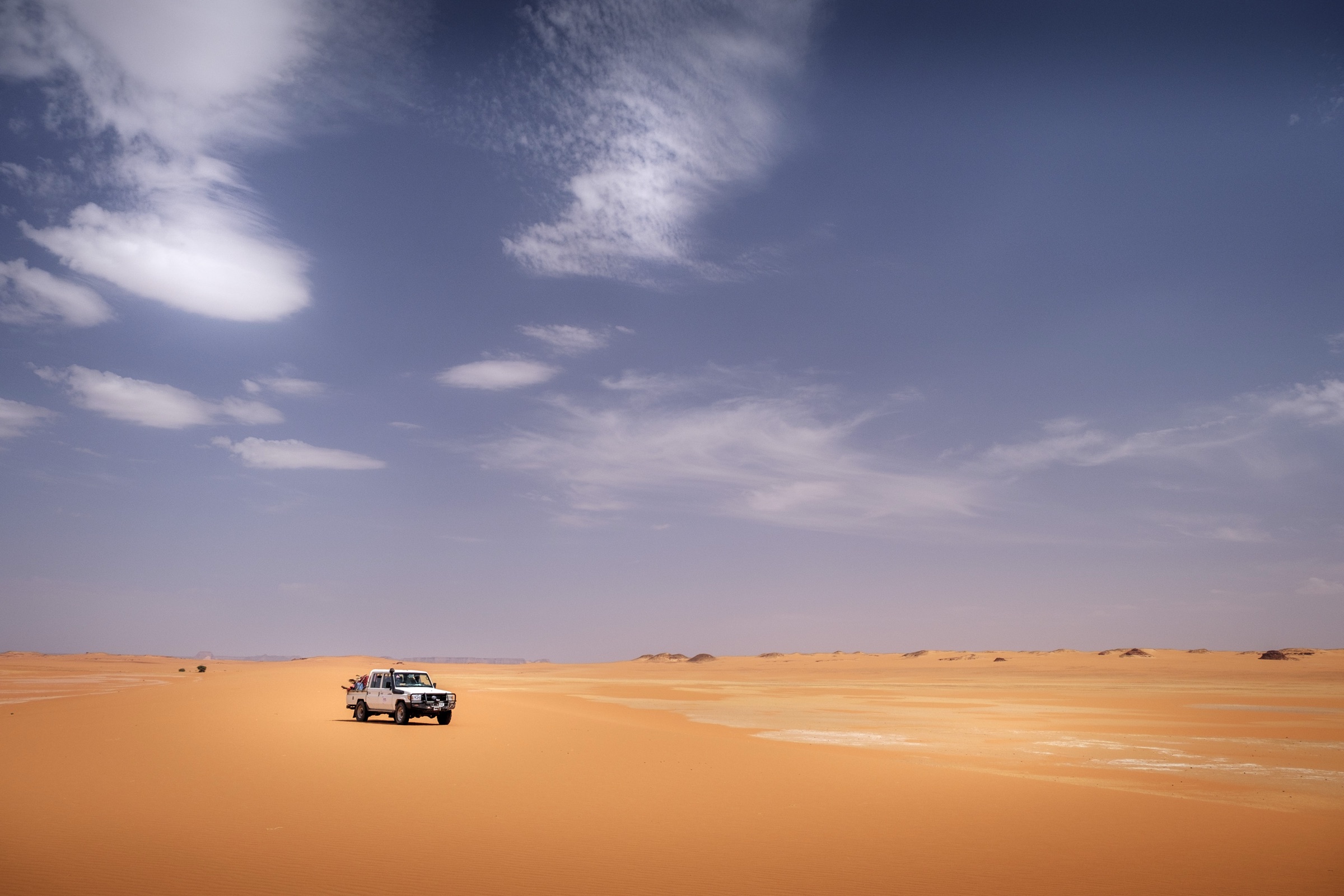 A vehicle crossing orange sand dunes beneath a wide sky in Chad.