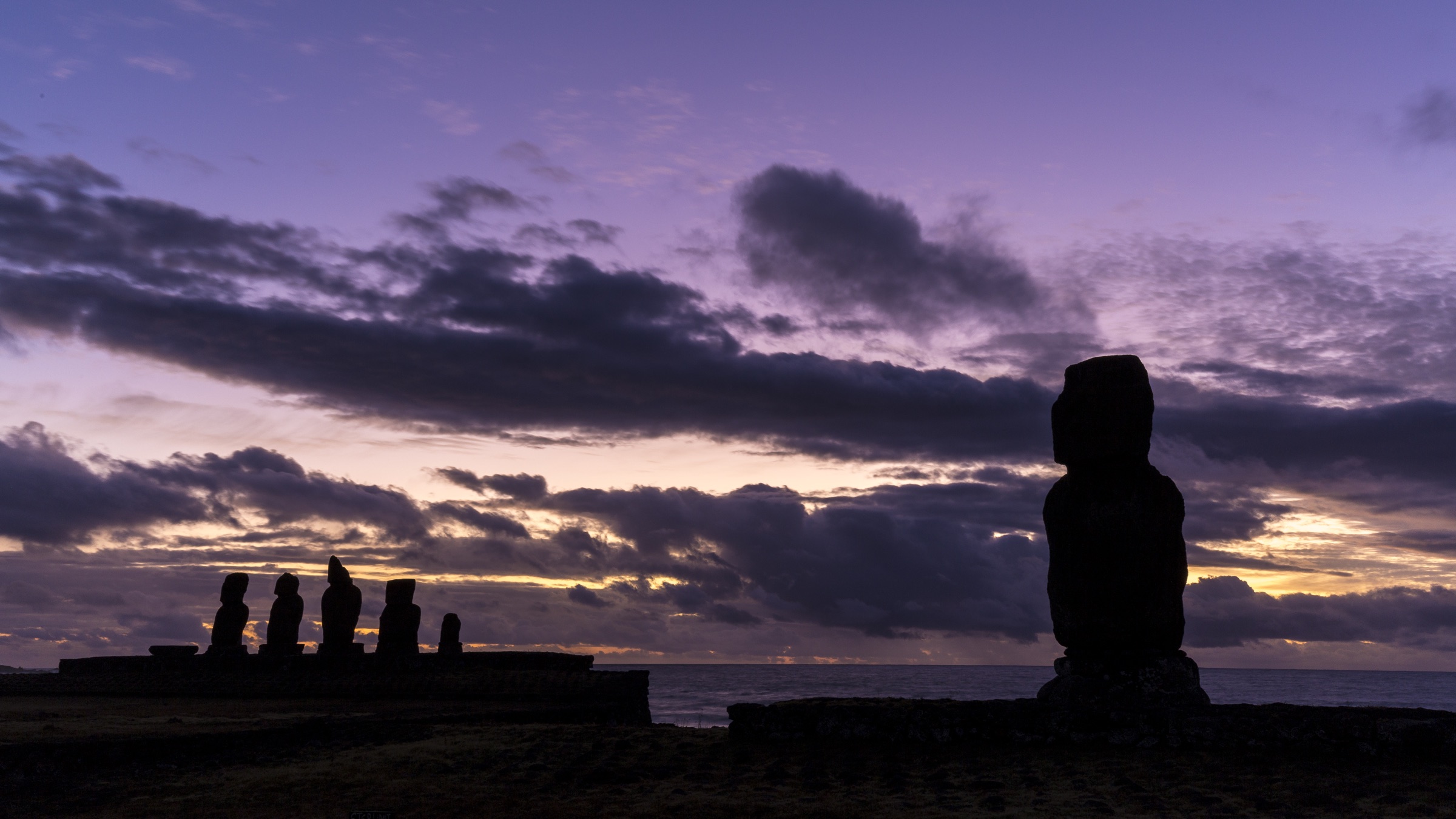 Silhouettes of moai statues beneath a colourful evening sky on Easter Island.