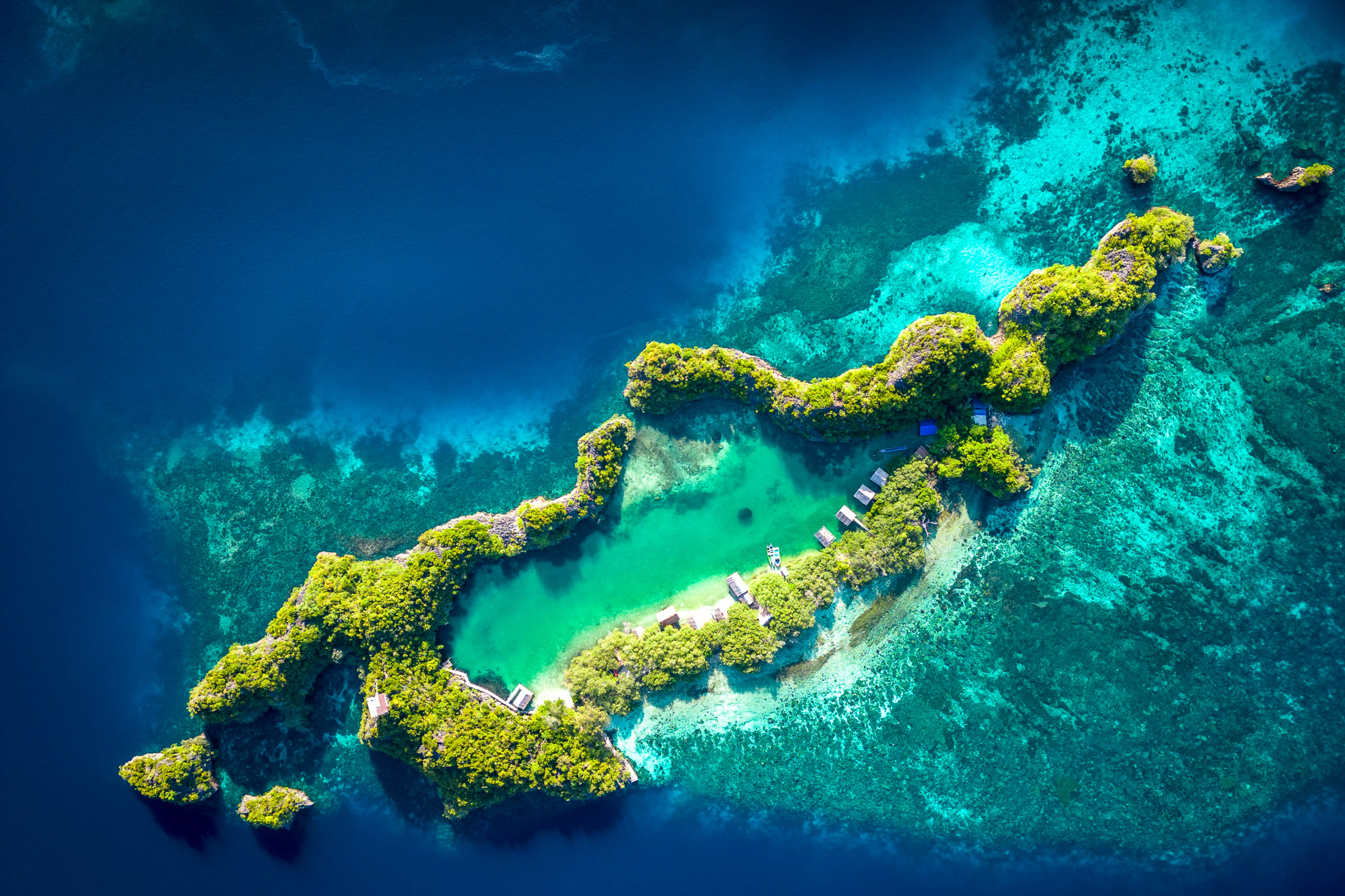 Aerial view of a small green island surrounded by turquoise reefs in Indonesia.