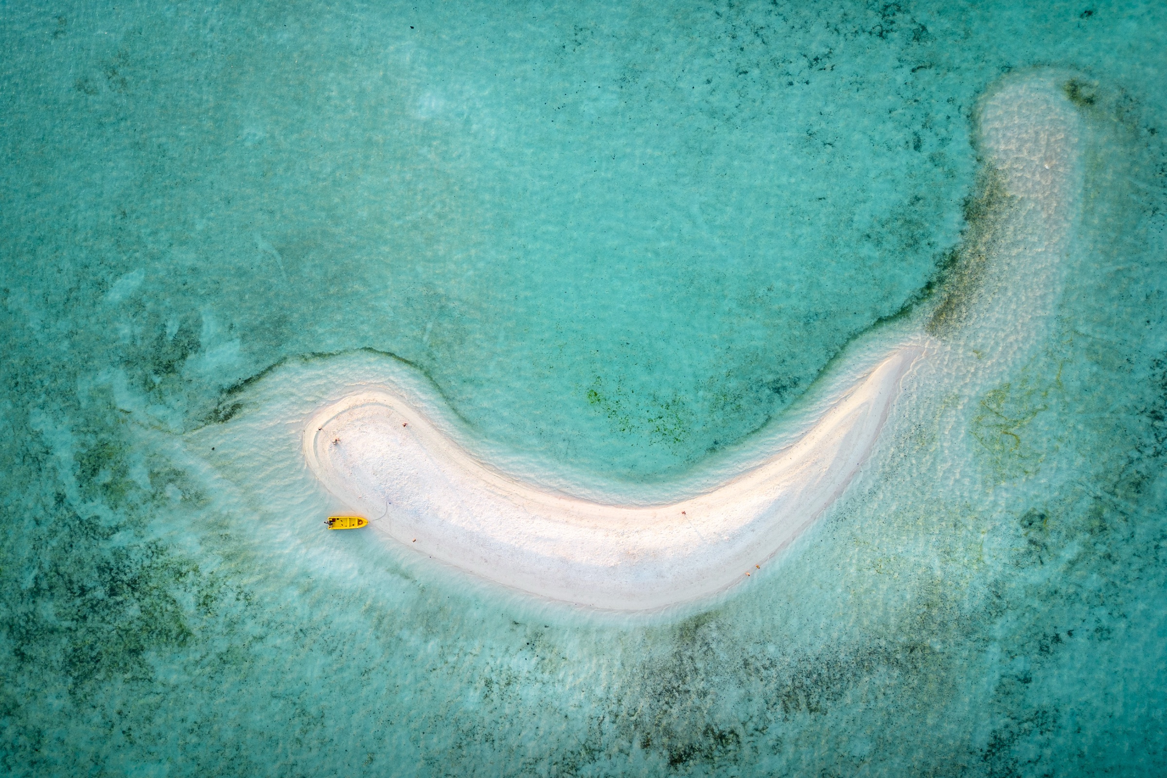 A curved white sandbar and a small boat in shallow turquoise water in Indonesia.