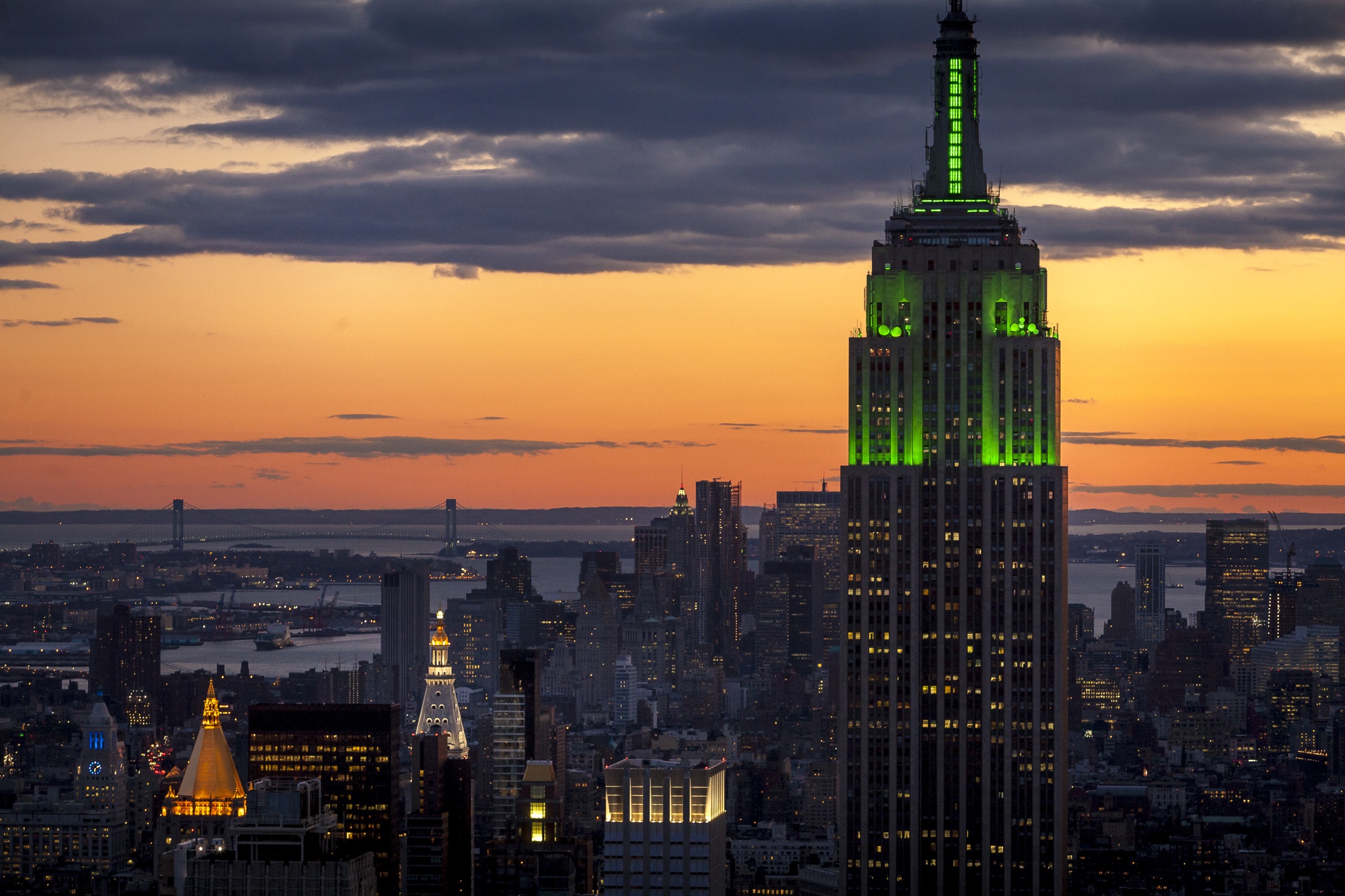The Empire State Building illuminated in green above New York at sunset.