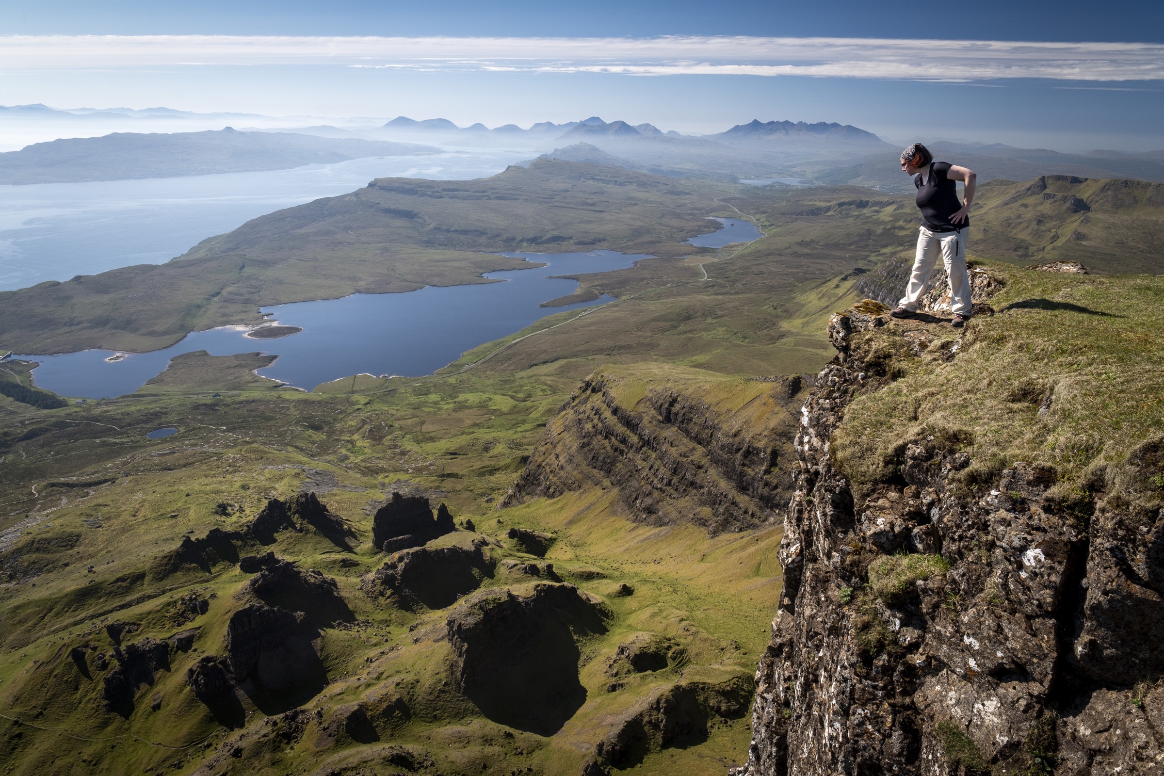 A traveller standing on a rocky clifftop above a coastal landscape in Scotland.