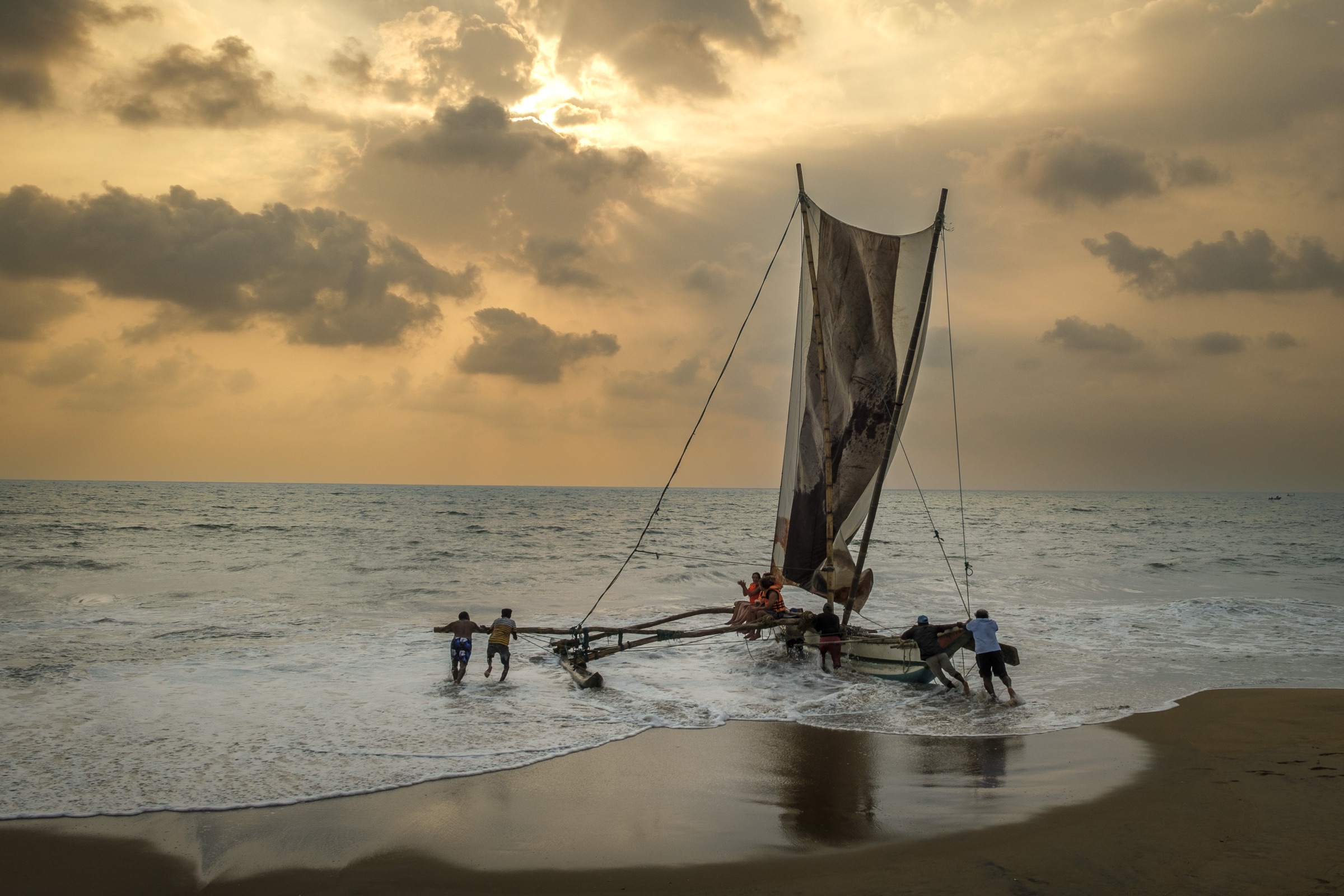 People launching a traditional sailboat through the surf in Sri Lanka.