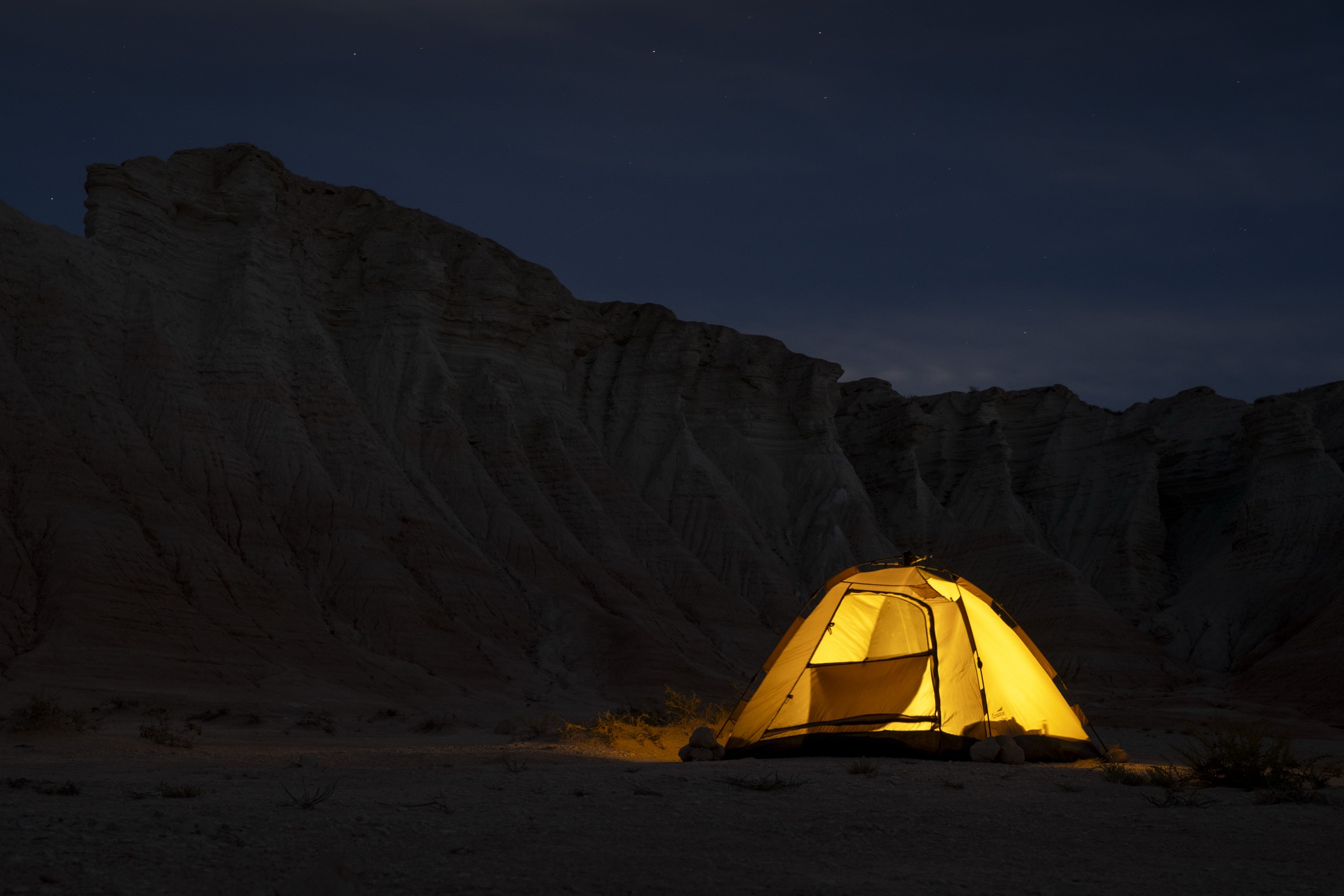 A glowing yellow tent beneath dark rock formations at night in Turkmenistan.