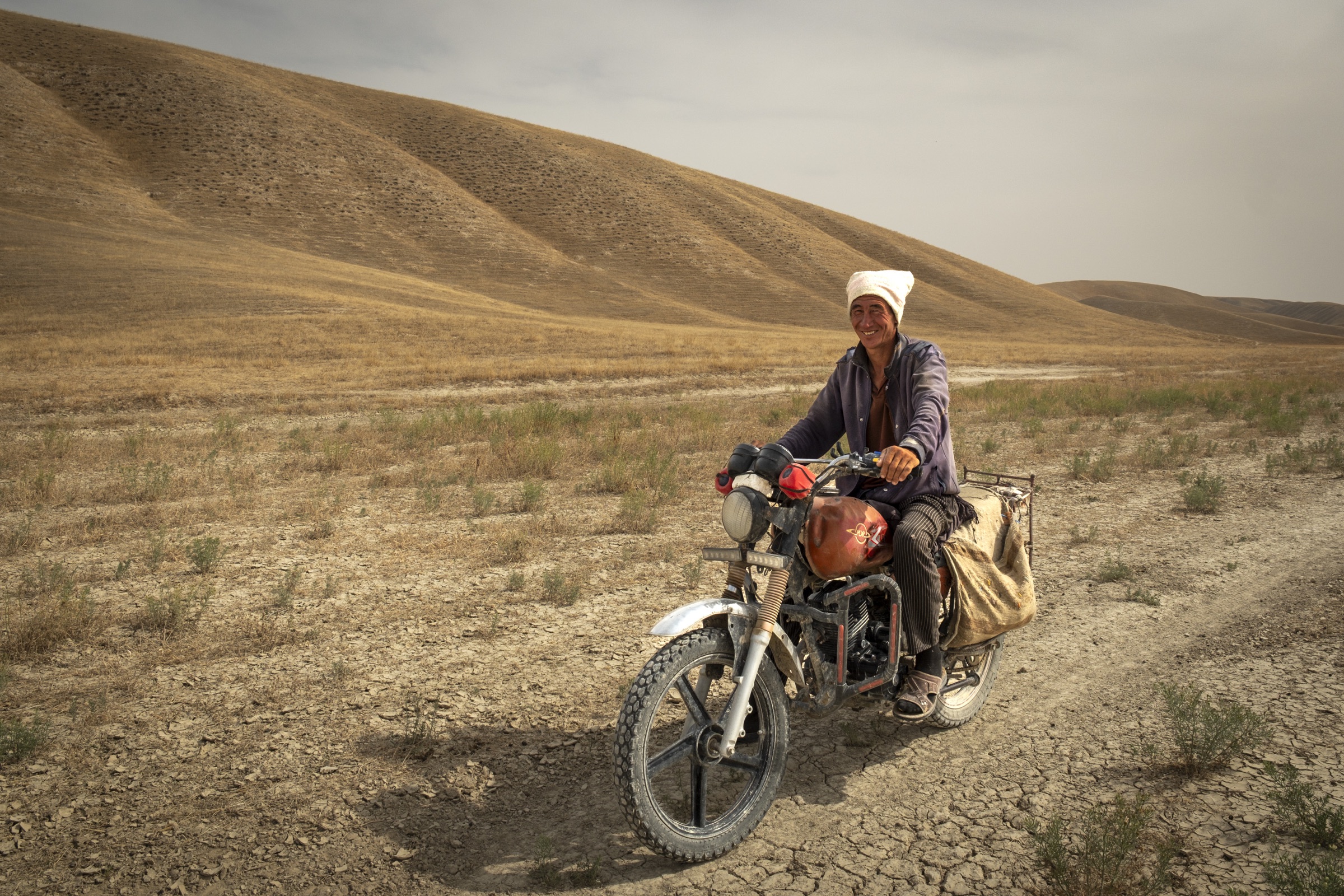 A motorcyclist crossing a grassy plain beneath bare hills in Turkmenistan.